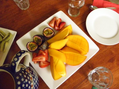 white square plate with mango, strawberries and passionfruit, jug of orange juice