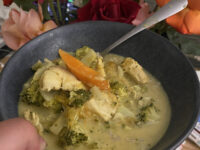 chicken mango curry in blue ceramic bowl with various colours of rose flowers behind