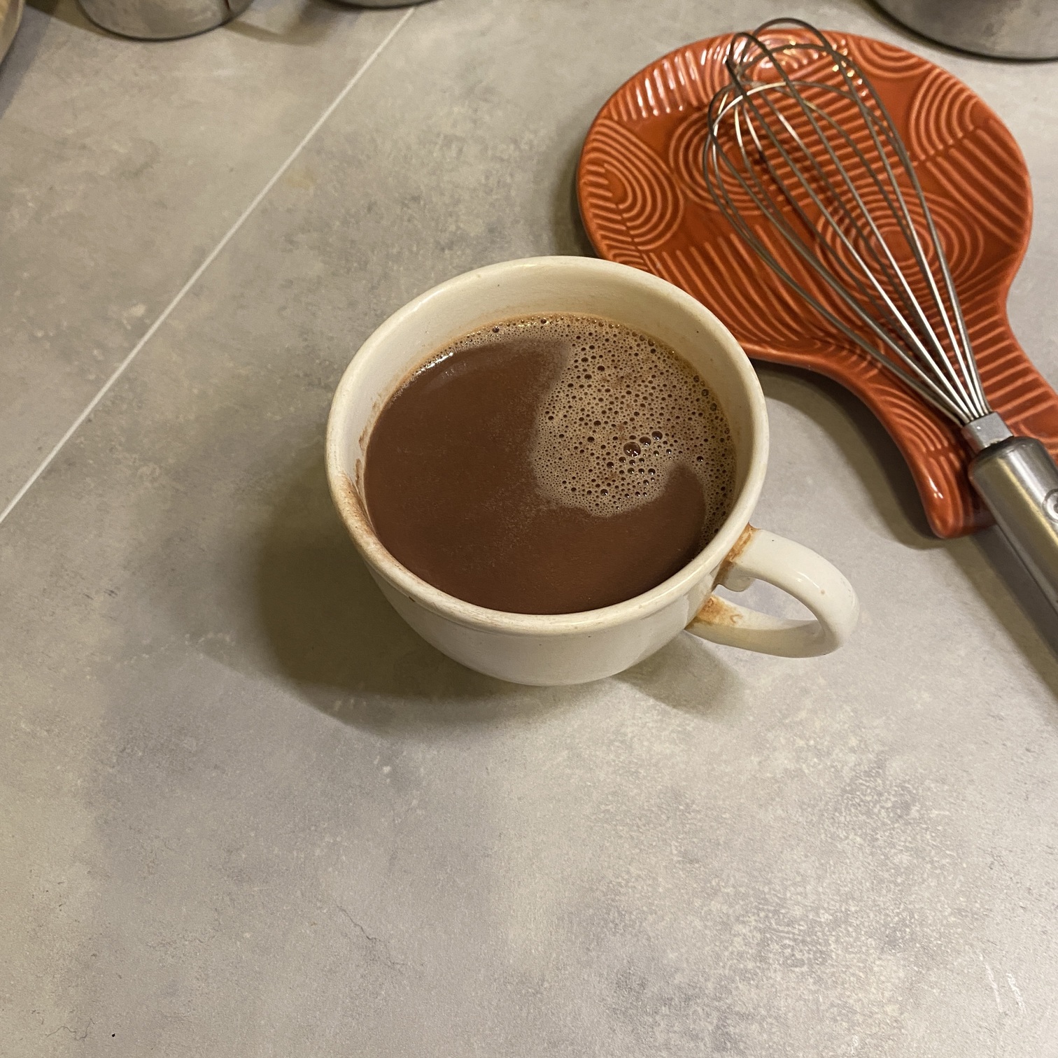 hot chocolate in a cup with a whisk and red spoon rest nearby
