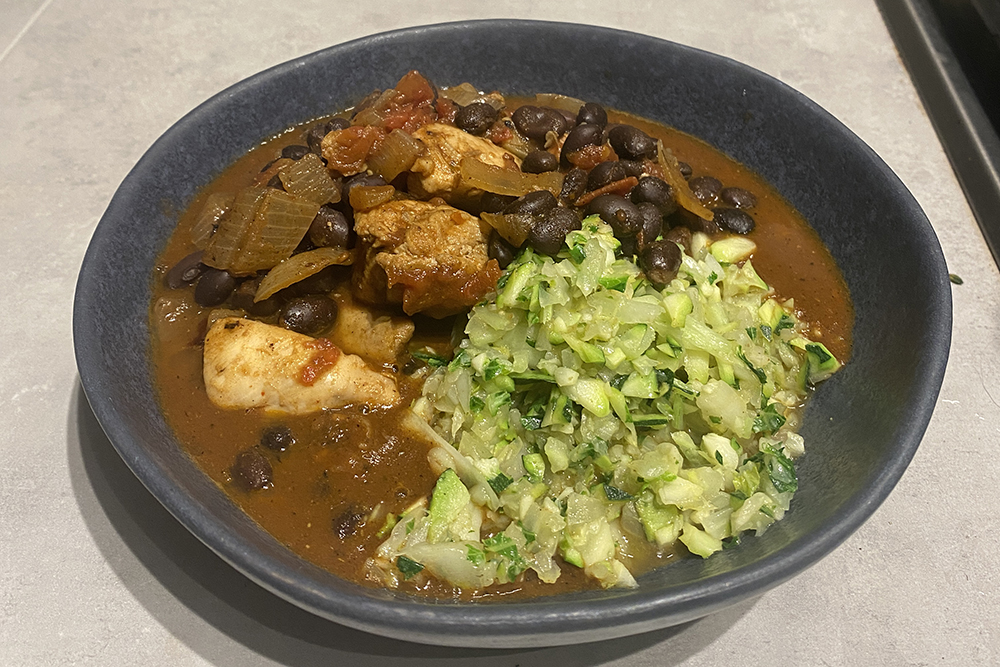 bowl with saucy stew and chunks of chicken next to green and white vegetable rice